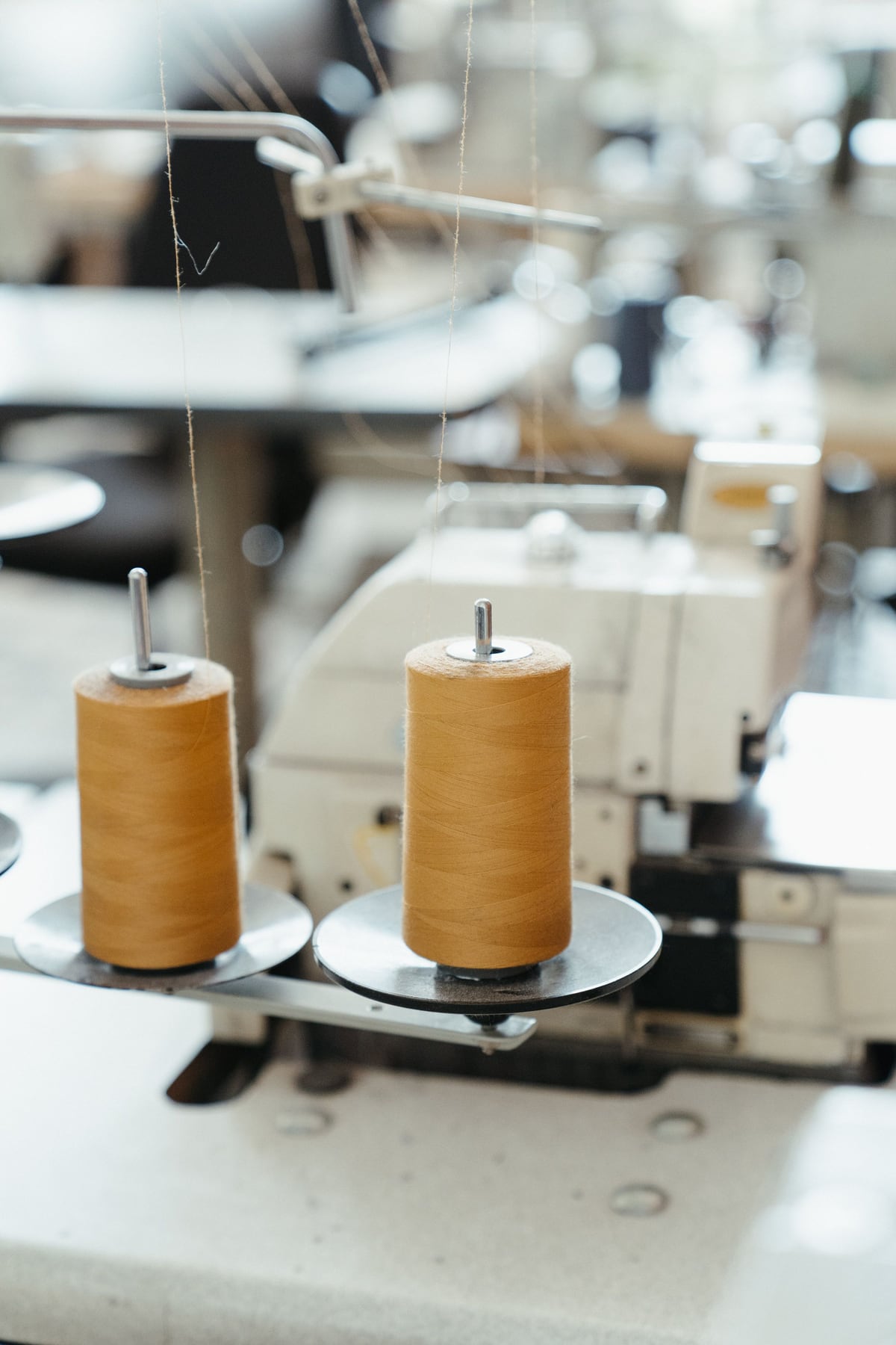Warm ochre thread spools on an industrial sewing machine in a bright workshop