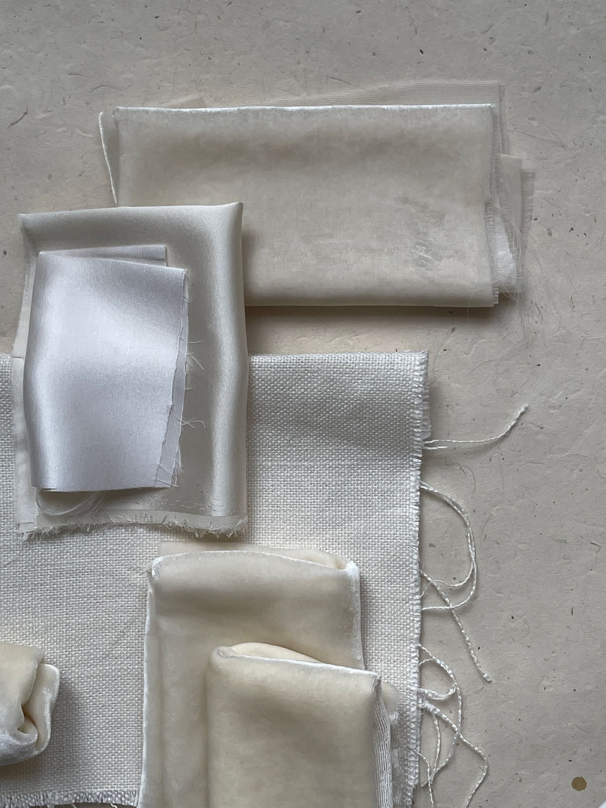 Layered cream, linen and silk fabric swatches showing varied textile textures